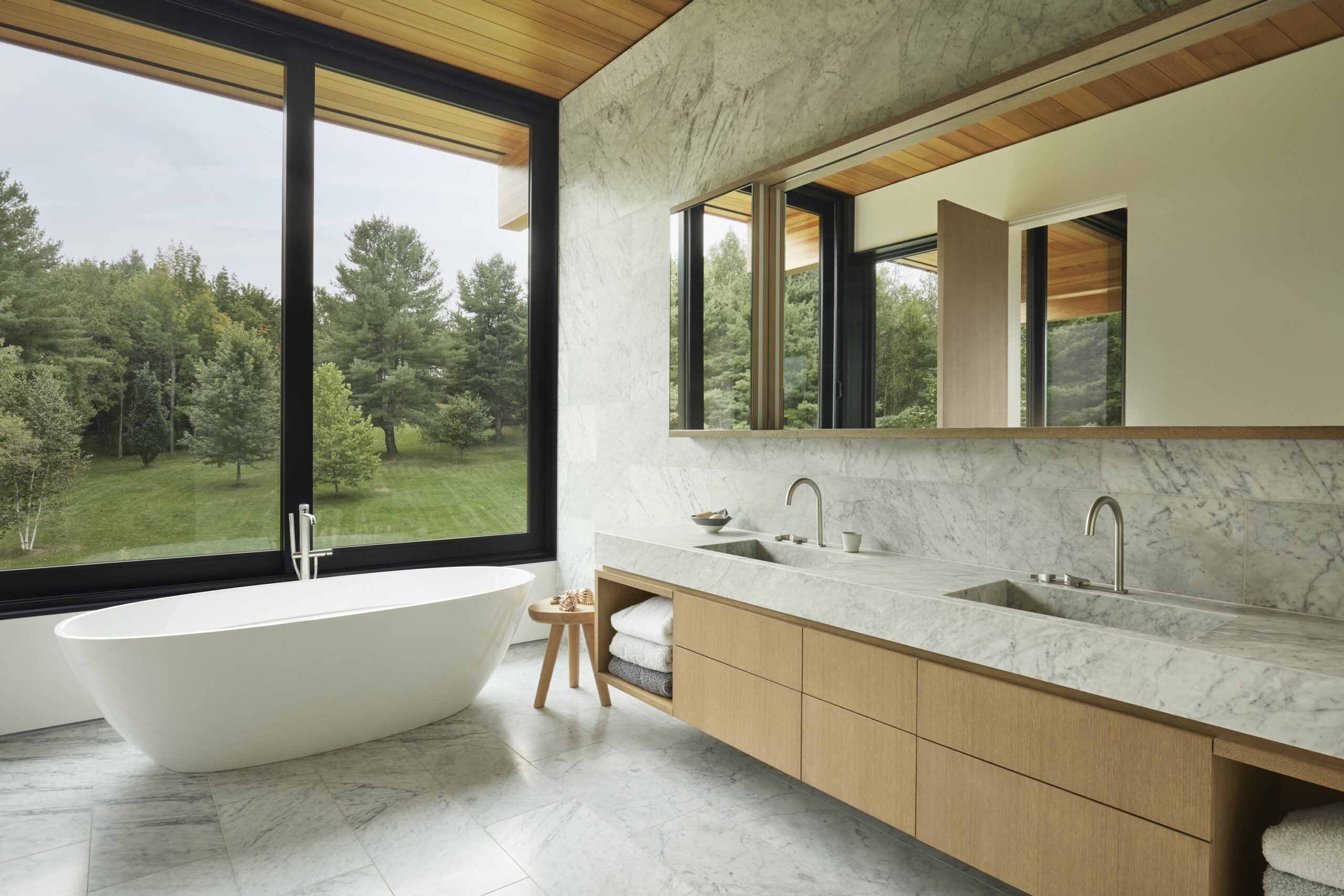 Bathroom with freestanding tub, double sinks, and view of forest landscape