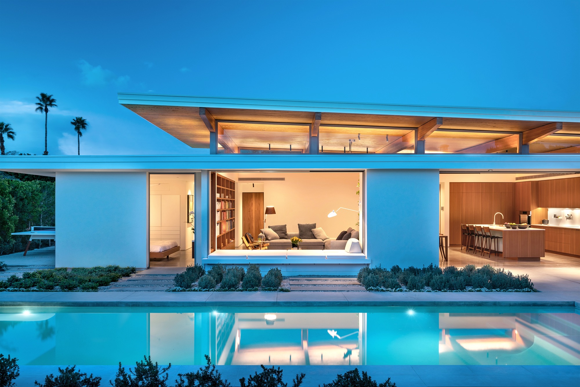 View of the interior of a modern custom prefab home from the outdoor pool and courtyard at night