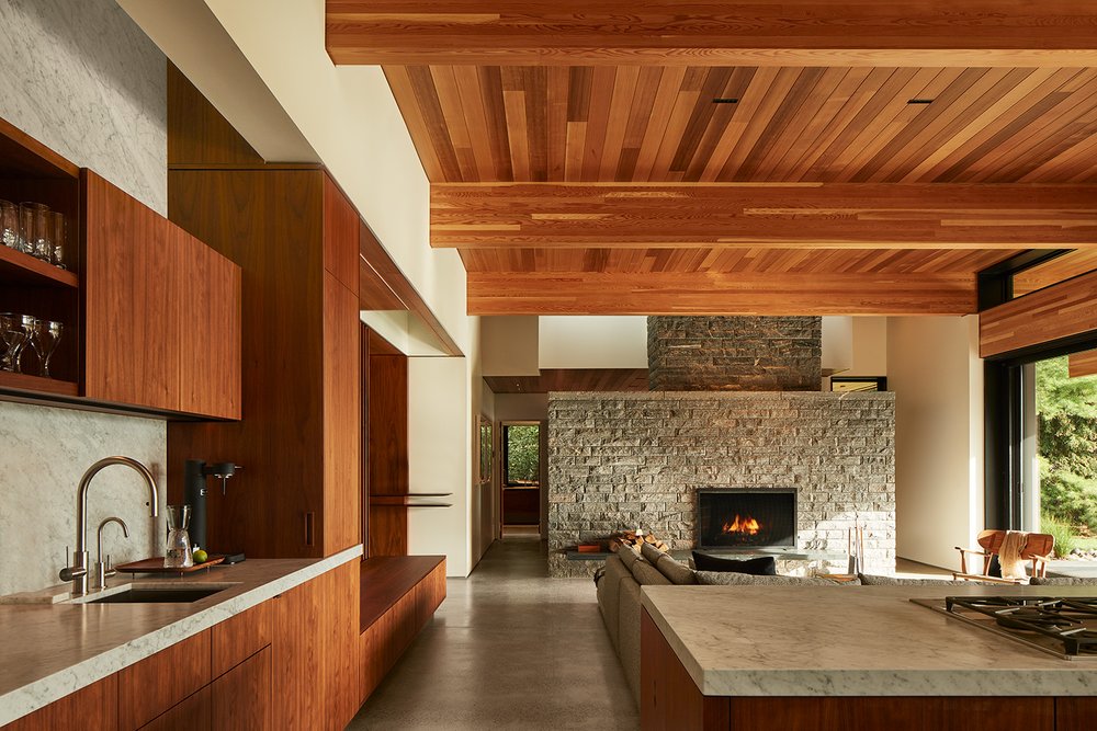 Gran salón con gabinetes de madera, isla de cocina y chimenea de piedra