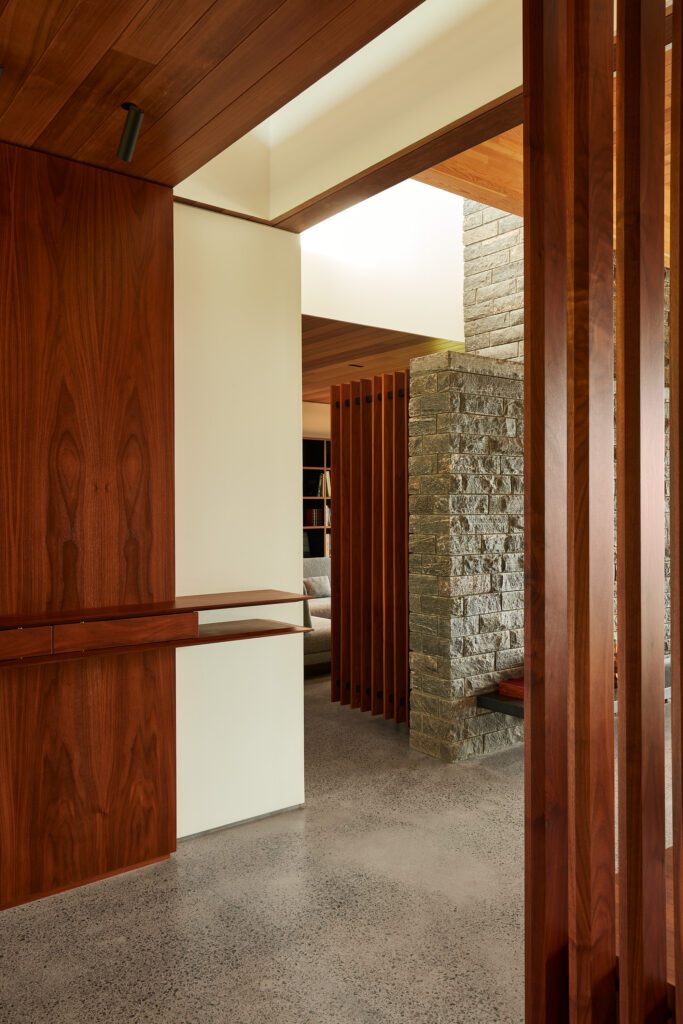 View of an office through a slatted wooden screen in a modern custom home with a stone wall
