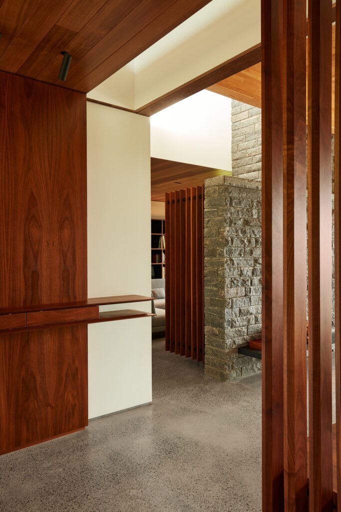 Vue d'un bureau à travers un paravent à lattes en bois dans une maison personnalisée moderne avec un mur en pierre