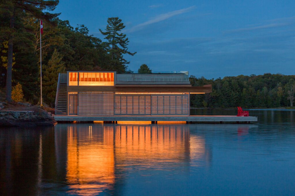 View of a modern wooden boathouse, lit from within, on a lake