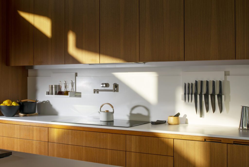 A modern kitchen counter with wooden cabinetry above and below, a bowl of lemons, a serving pot, a kettle, a mortal and pestle, a knife block, and a pitcher