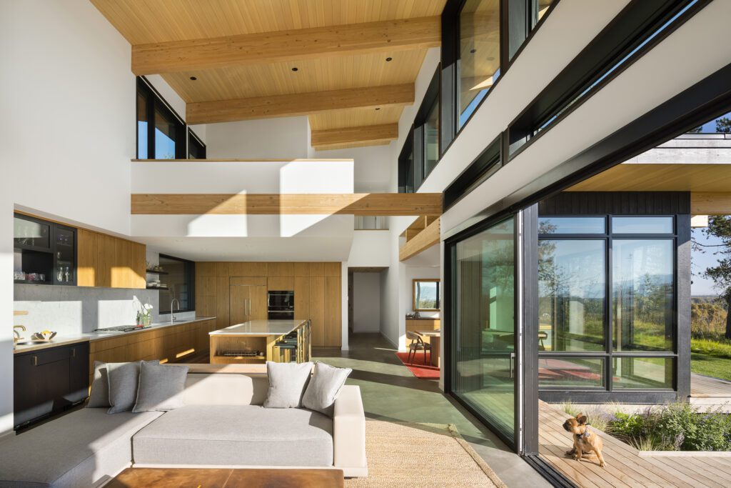 View of the kitchen and dining area in the double-height great room of a sun-filled modern home