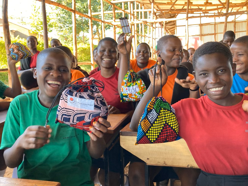 Girls in a school in Uganda smile while displaying their reusable, washable menstrual kits