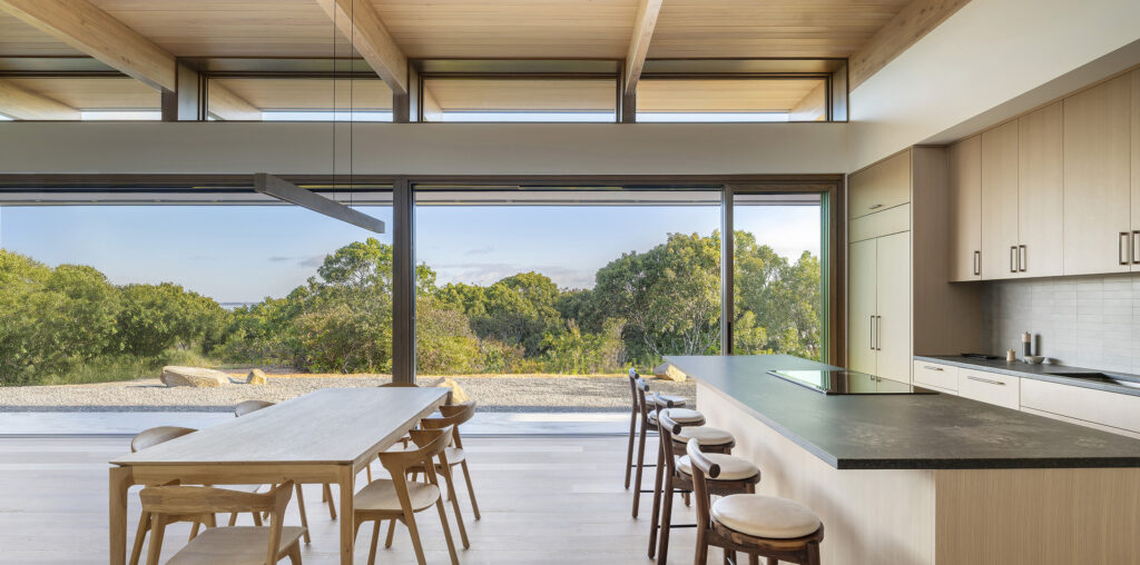 Dining area and kitchen of an open, airy modern home with a view out to trees and ocean