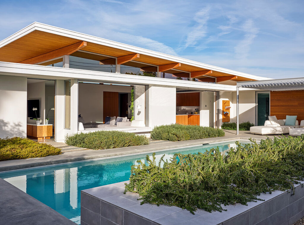 Vista exterior de una casa moderna en el desierto con piscina y jardín en primer plano.